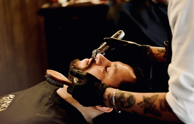 Hombre sentado en la silla de una barbería mientras un barbero le está definiendo la barba