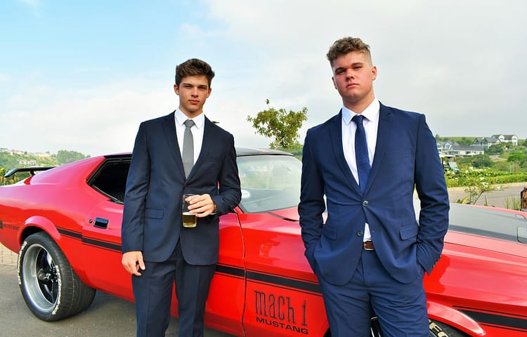 Two young men getting ready for their matric dance (prom) posing next to a classic red Ford Mustang and looking suave!